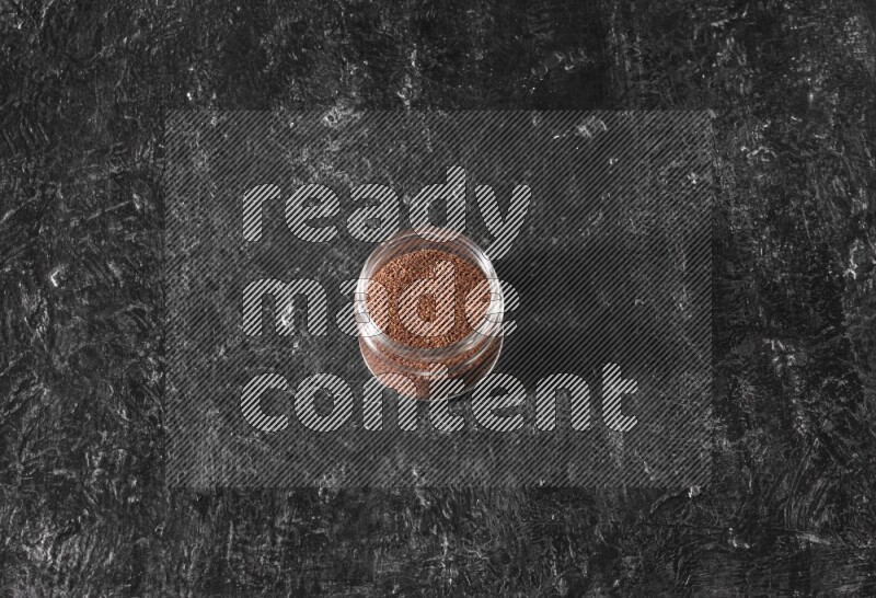 A glass jar full of garden cress seeds on a textured black flooring