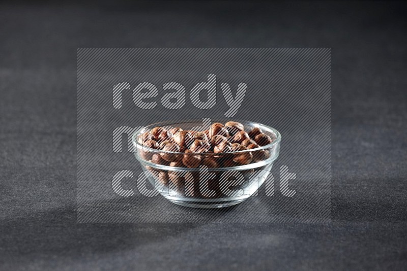 A glass bowl full of peeled hazelnuts on a black background in different angles