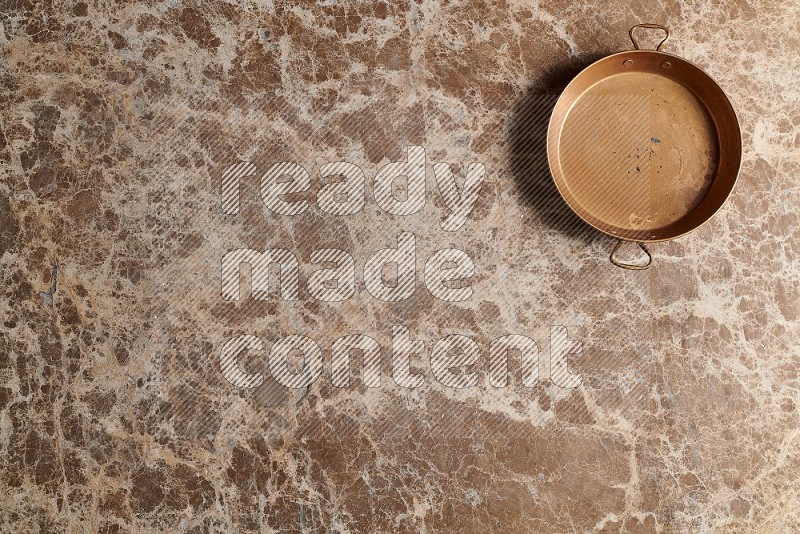 Top View Shot Of A Small Copper pan On beige Marble Flooring