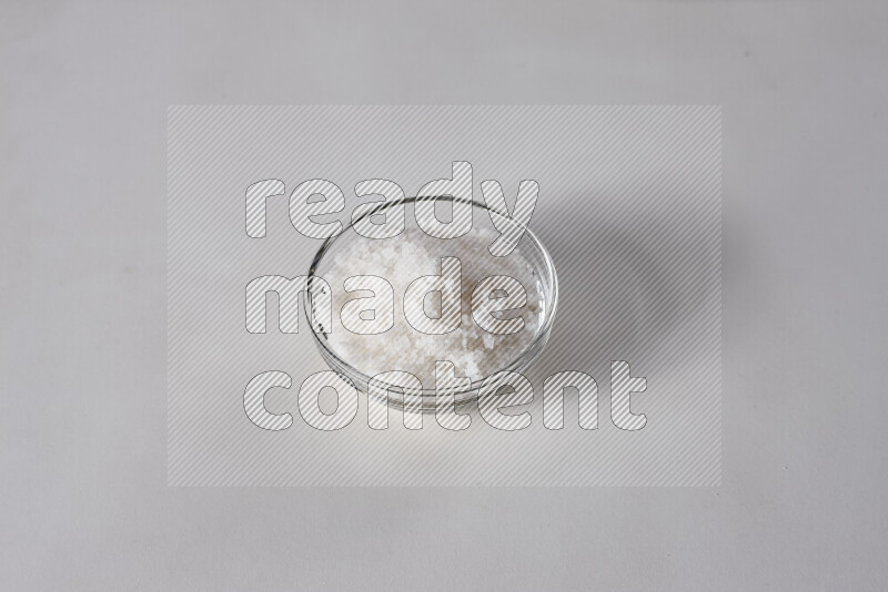 A glass bowl full of coarse sea salt crystals on white background