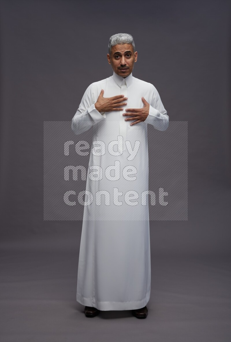 Saudi man wearing thob standing interacting with the camera on gray background