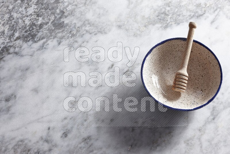 وعاء فخاري متعدد الألوان مع ملعقة عسل خشبية بداخله على خلفية من الرخام الرمادي