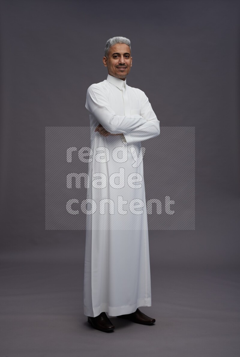 Saudi man wearing thob standing with crossed arms on gray background