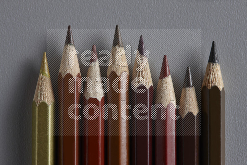 A collection of colored pencils arranged showcasing a gradient of brown hues on grey background