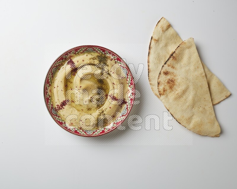 Hummus in a red plate with patterns garnished with zaatar & sumak on a white background