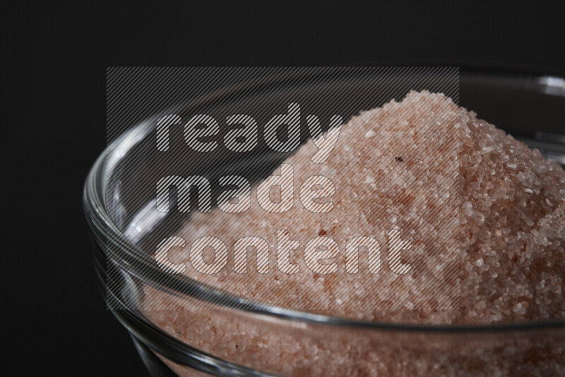 A glass bowl full of fine himalayan salt on black background