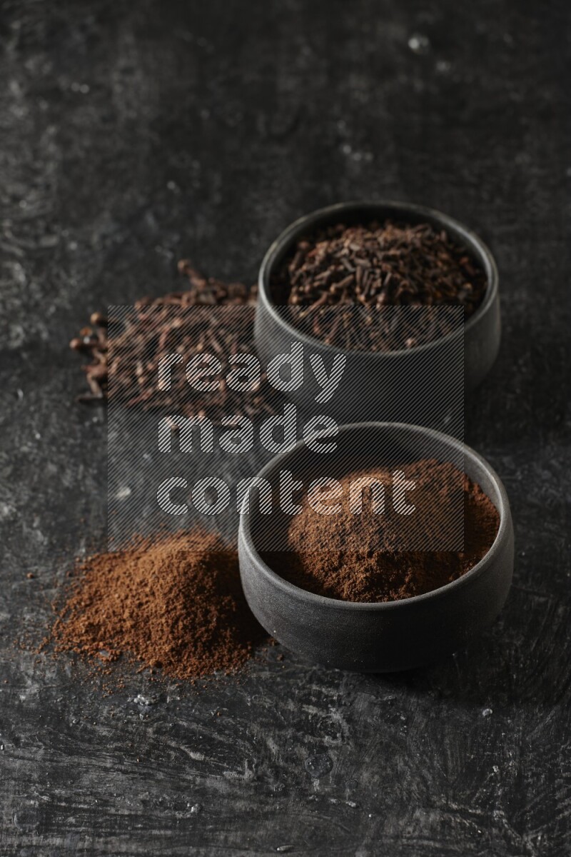 وعاءين من الفخار الأسود أحدهما ممتلئي بحبوب القرنفل والآخر ممتلئ ببودرة القرنفل على خلفية سوداء