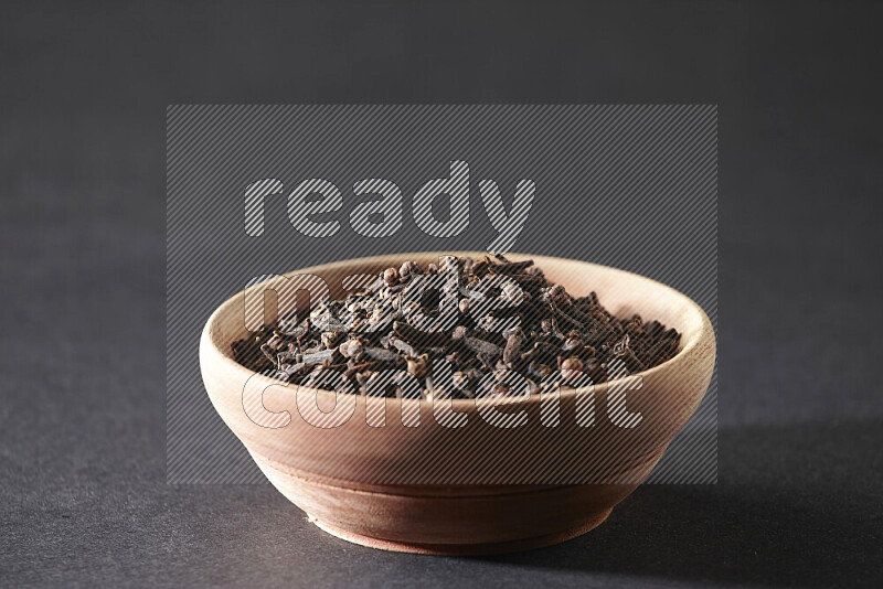 A wooden bowl full of cloves on a black flooring