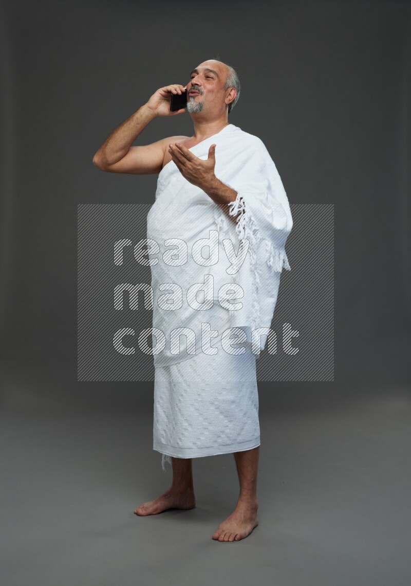 A man wearing Ehram Standing talking on phone on gray background