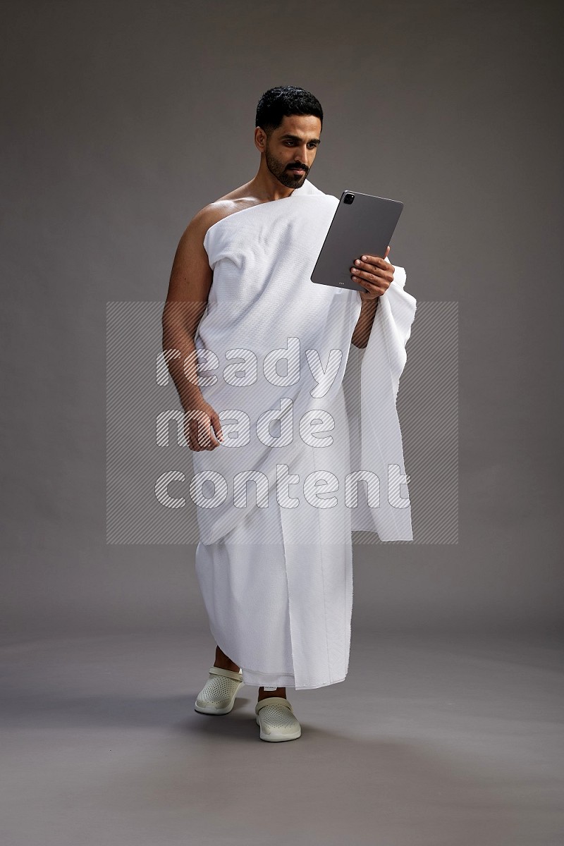 A man wearing Ehram and holding a tablet on gray background