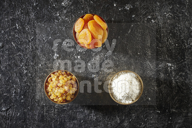 Dried fruits in metal bowls in a dark setup