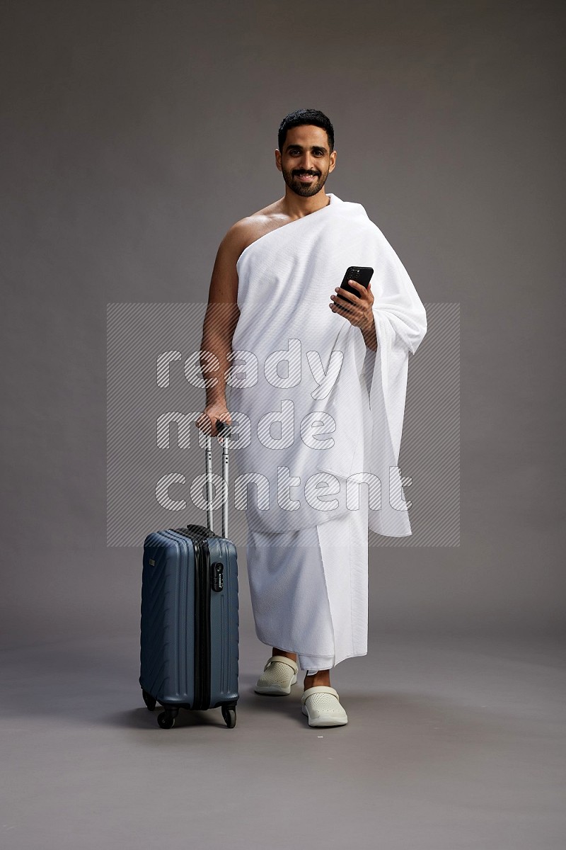 A man wearing Ehram Standing holding traveling bag on gray background