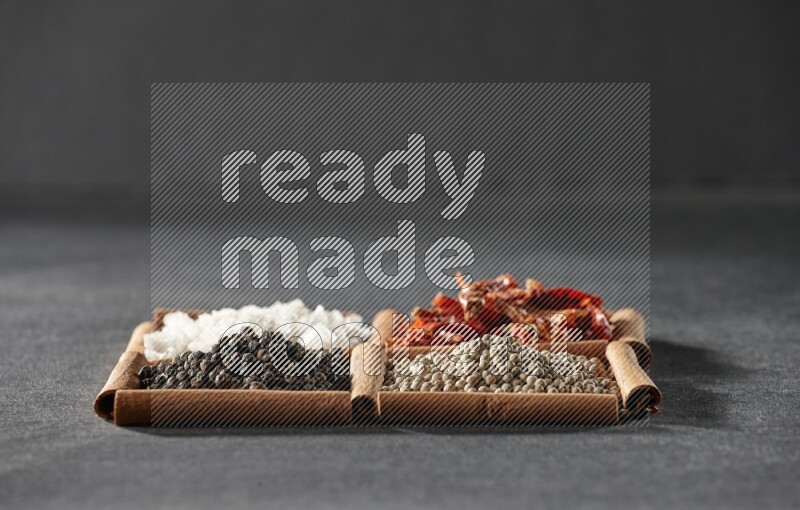 4 squares of cinnamon sticks full of black pepper, white pepper, dried red chilis and white salt on black flooring