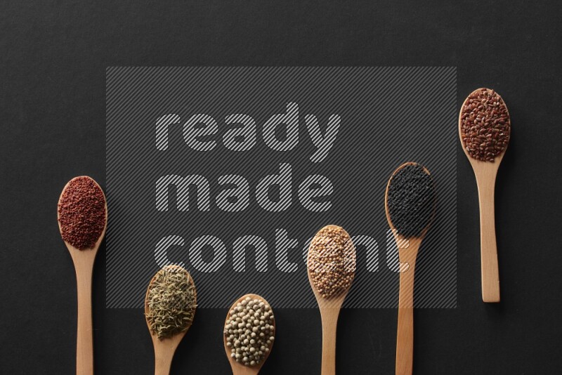 الفلفل الأسود وحبوب الخردل وحبة البركة وحب الرشاد والكمون و حبوب الكتان في معالق خشبية علي خلفية سوداء