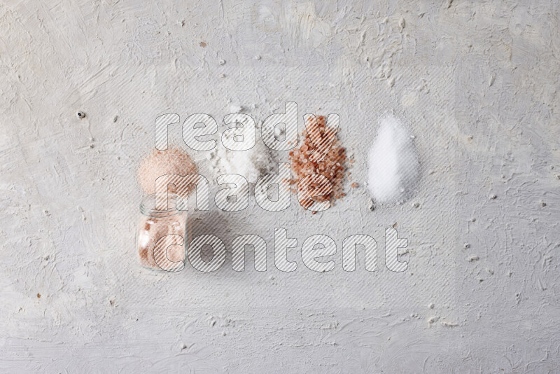 4 glass jars filled with table salt, coarse sea salt, fine himalayan salt and coarse himalayan salt on white background