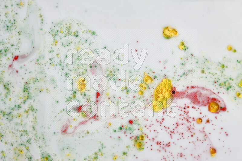 The image captures a splatter of yellow, red and green paint over a white backdrop