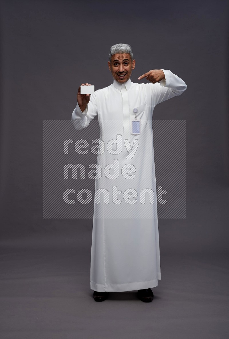 Saudi man wearing thob with pocket employee badge standing holding ATM card on gray background