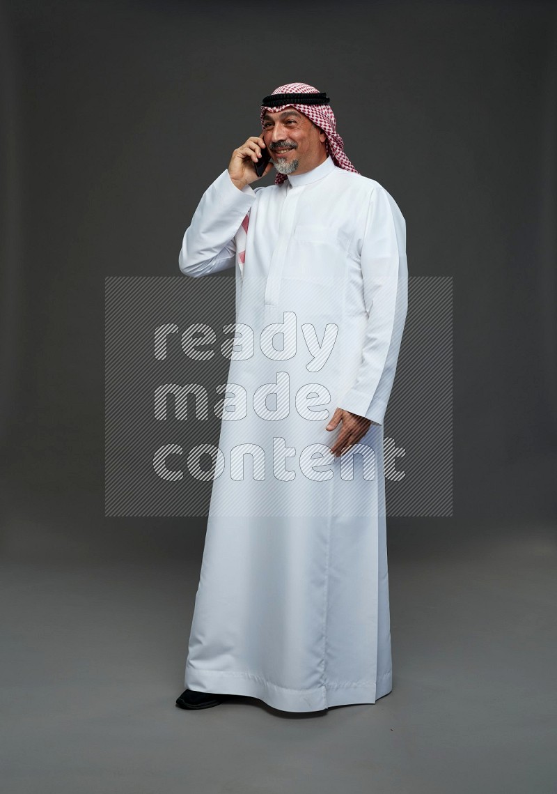 Saudi man with shomag Standing talking on phone on gray background