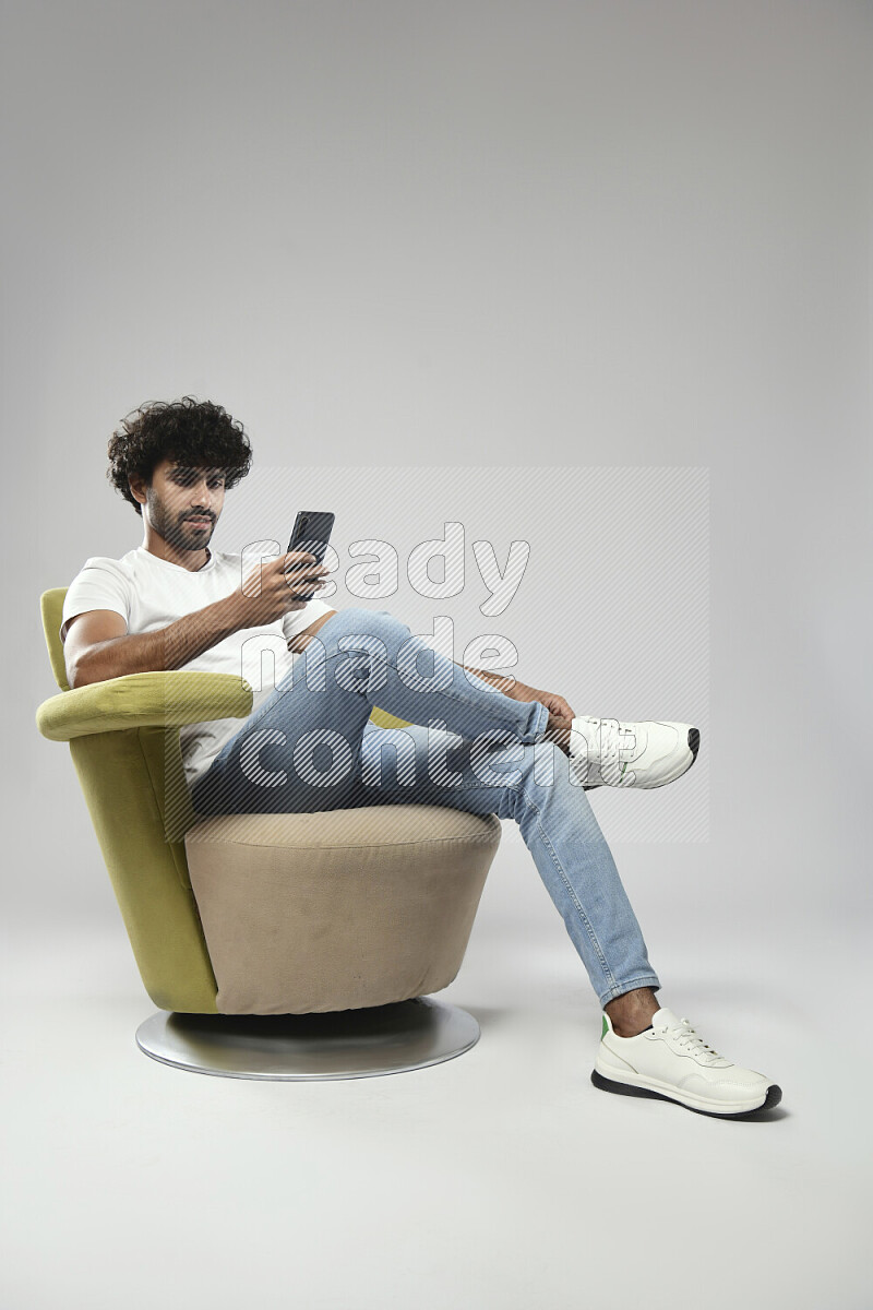رجل يرتدي ملابس كاجوال يجلس علي كرسي و يتصفح الهاتف علي خلفية بيضاء