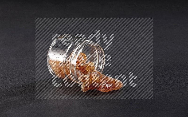 A glass jar full of gum arabic and jar is flipped and gum arabic spread out on black flooring in different angles