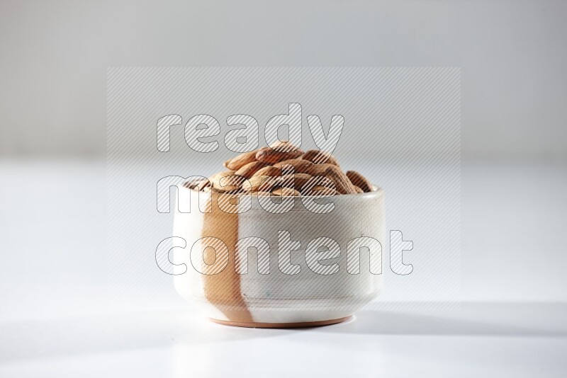 A beige ceramic bowl full of peeled almonds on a white background in different angles