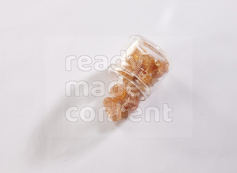 A glass jar full of gum arabic and jar is flipped with fallen pieces spread out on white flooring