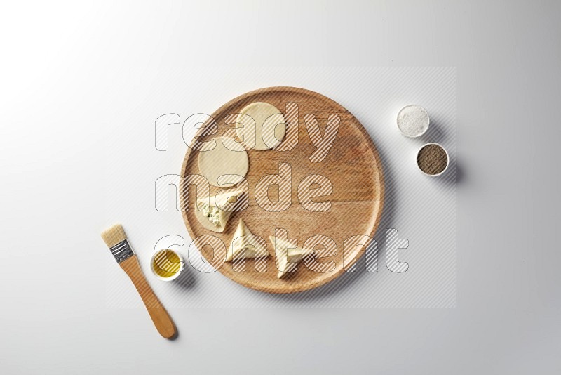 two closed sambosas and one open sambosa filled with cheese while salt, black pepper and oil with oil brush aside in a wooden dish on a white background