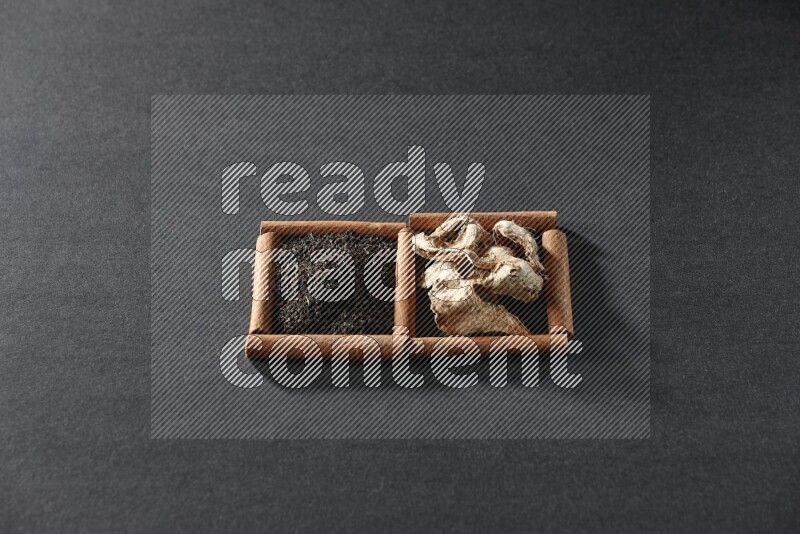 مربعان من أعواد القرفة ممتلئان بالزنجبيل المجفف والشاي الأسود علي خلفية سوداء