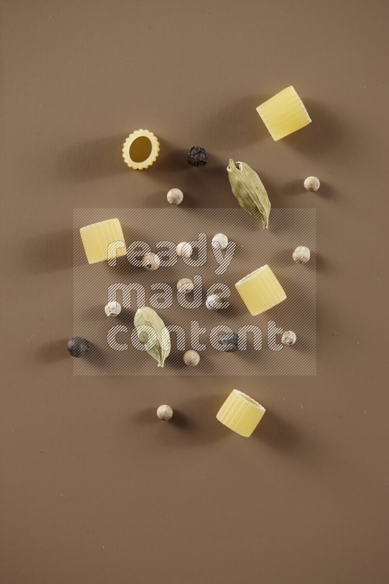 Raw pasta with different ingredients such as cherry tomatoes, garlic, onions, red chilis, black pepper, white pepper, bay laurel leaves, rosemary and cardamom on beige background