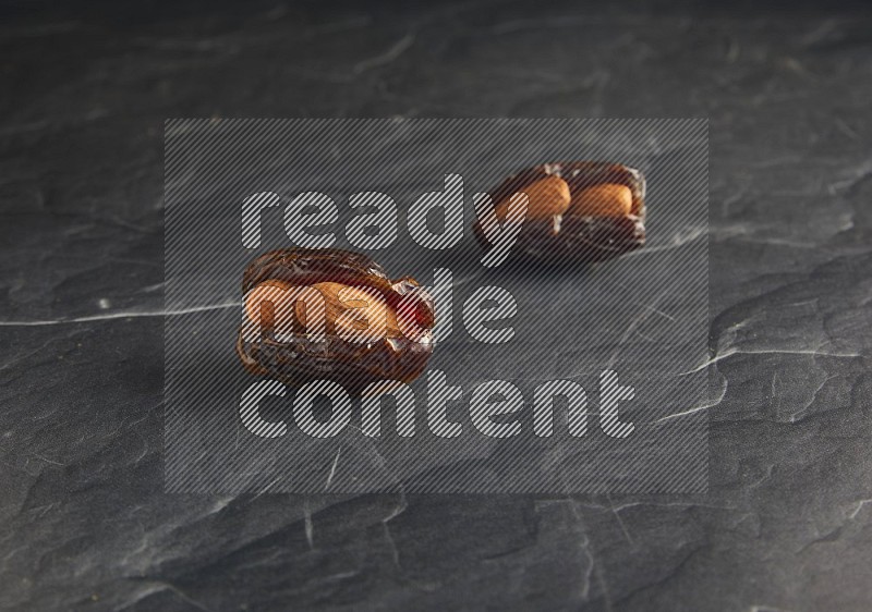 two almond stuffed madjoul dates on a black textured background