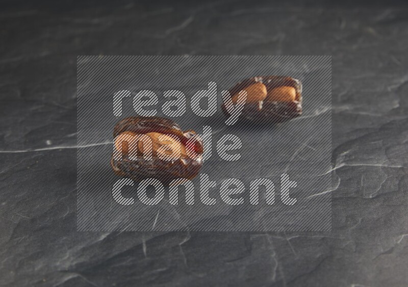 two almond stuffed madjoul dates on a black textured background