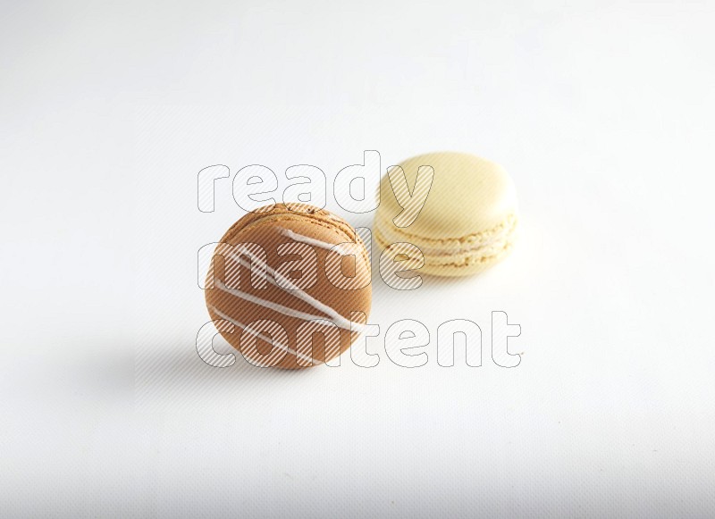 45º Shot of of two assorted Brown Irish Cream, and Yellow Vanilla macarons on white background