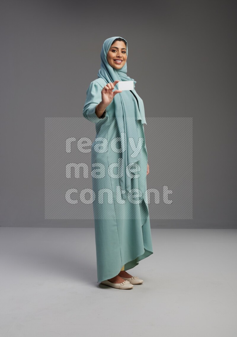 Saudi Woman wearing Abaya standing holding ATM card on Gray background