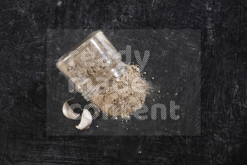 A glass jar full of garlic powder flipped over with the powder came out on a textured black flooring