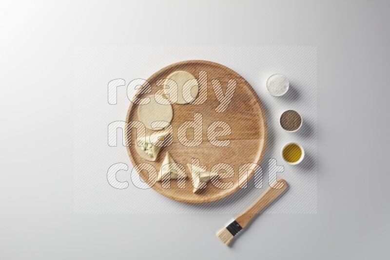 two closed sambosas and one open sambosa filled with cheese while salt, black pepper and oil with oil brush aside in a wooden dish on a white background