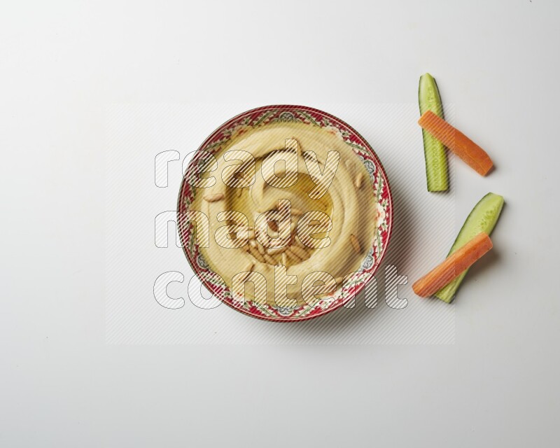 Hummus in a red plate with patterns garnished with pine nuts on a white background