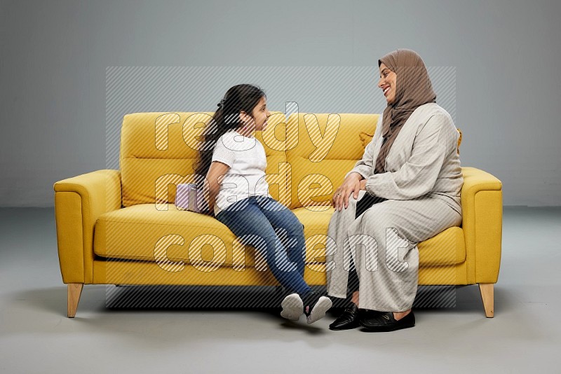 A girl sitting hiding a gift behind her back for her mother on gray background