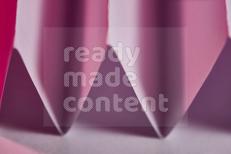 A close-up abstract image showing sharp geometric paper folds in pink gradients