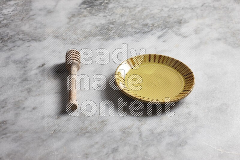 Multicolored pottery plate with wooden honey dipper on the side on grey marble background