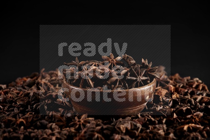 Star Anise in a wooden bowl and surrounded by more anise filling the frame on black flooring