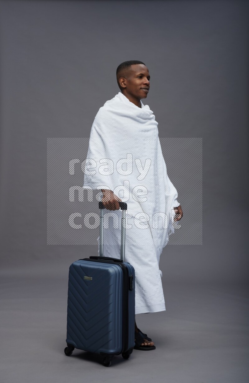 A man wearing Ehram Standing holding traveling bag on gray background