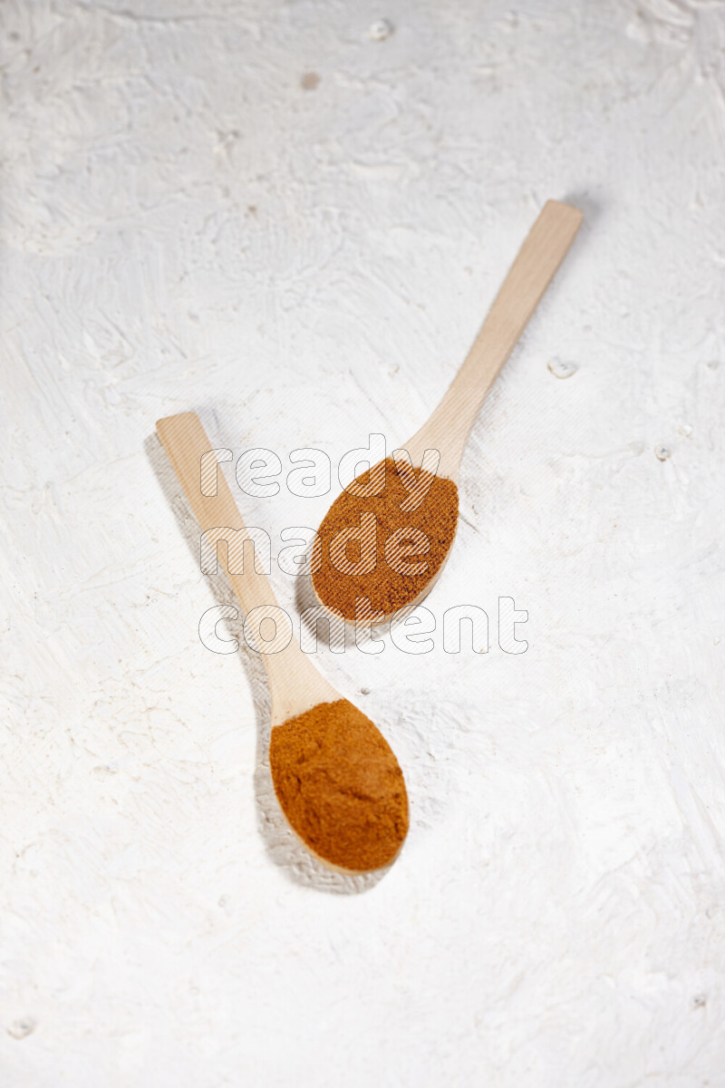 Two wooden spoons full of ground paprika powder on white background