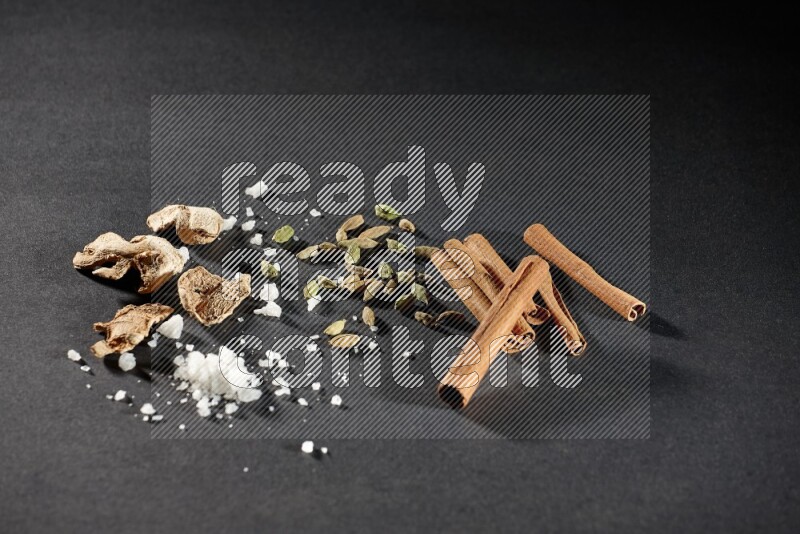 Ginger, salt, cardamom and cinnamon sticks on black flooring