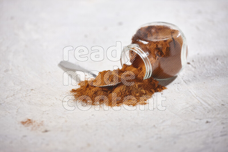 A glass jar full of ground paprika powder flipped with some spilling powder on white background