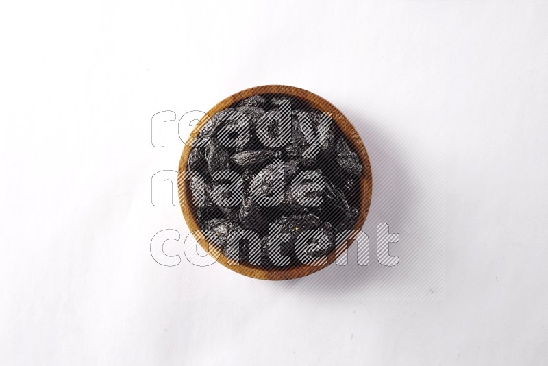 Dried plums in a wooden bowl on white background