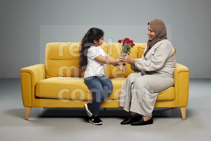 A girl sitting giving flowers to her mother on gray background