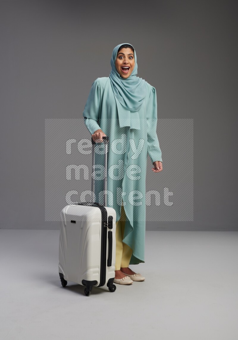 Saudi Woman wearing Abaya standing holding Travel bag on Gray background
