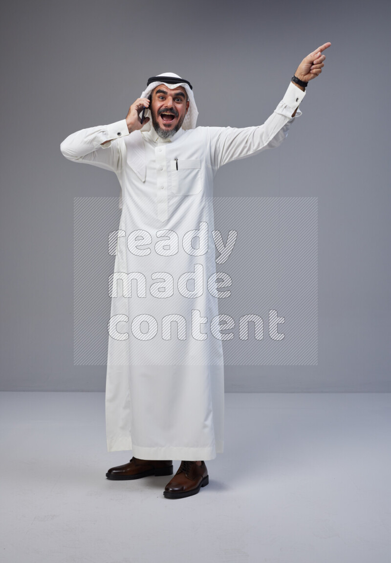 Saudi man Wearing Thob and white Shomag standing talking on phone on Gray background