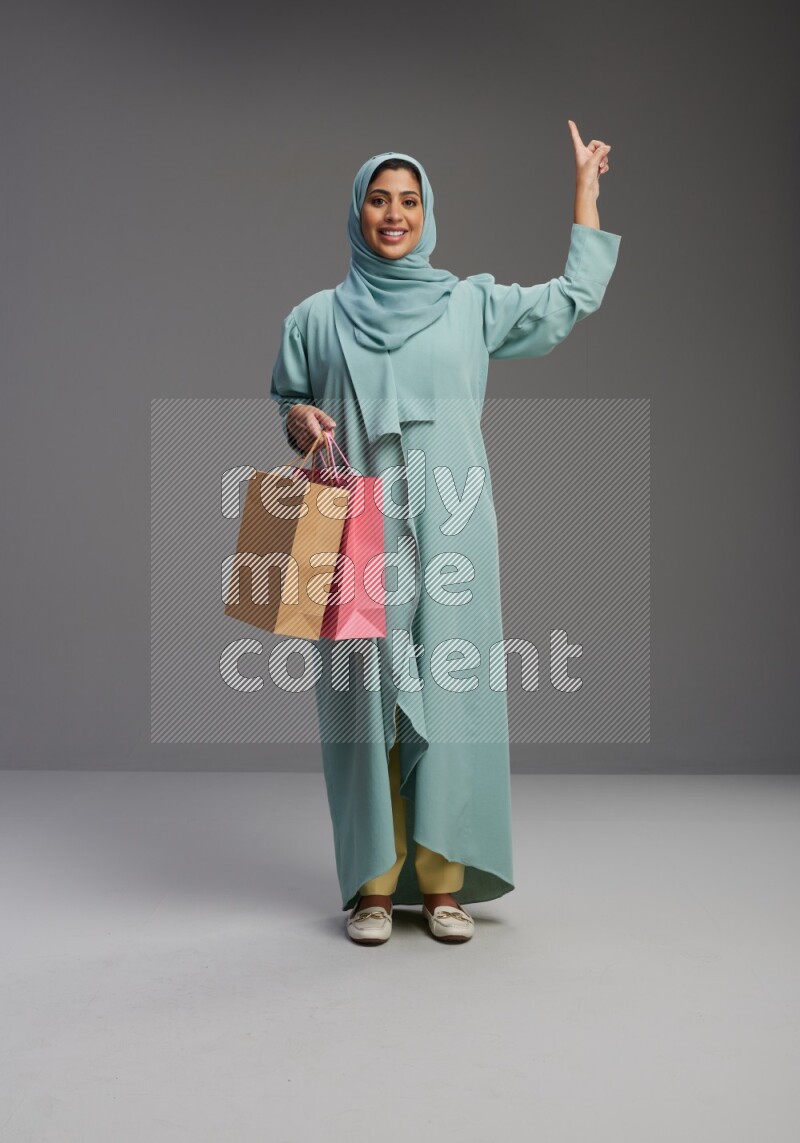 Saudi Woman wearing Abaya standing holding shopping bag on Gray background