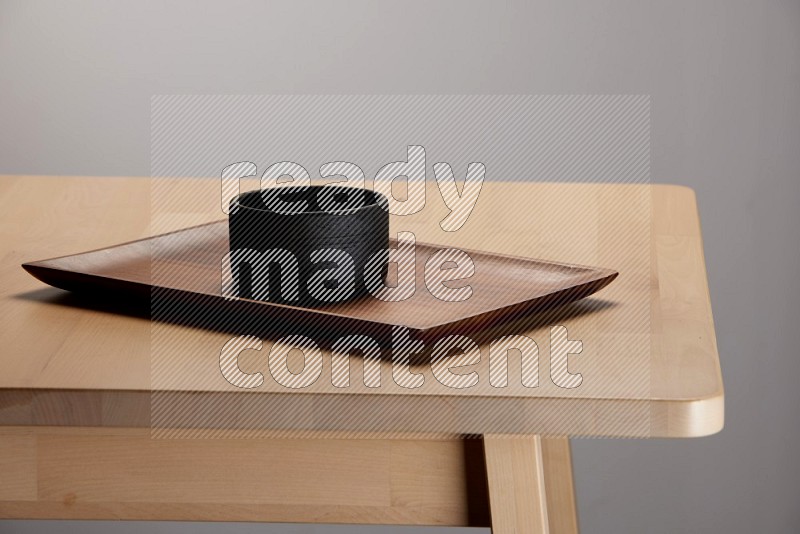 black bowl placed on a rectangular wooden tray on the edge of wooden table